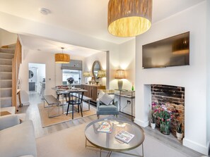 A modern living room with a fireplace, a TV mounted on the wall, and a dining area with a kitchen in the background. - 3 bedroom accommodation in Lowestoft (Lowestoft)