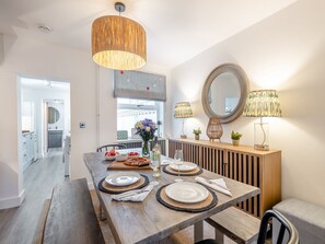 A dining area with a wooden table set for four, a hanging light fixture, and a large mirror on the wall. - 3 bedroom accommodation in Lowestoft (Lowestoft)