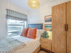 A bedroom with a bed, a bedside table with a lamp, a wardrobe, and a window with curtains. - 3 bedroom accommodation in Lowestoft (Lowestoft)
