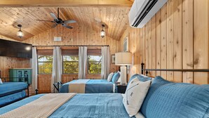 A cabin-style bedroom with two beds, wooden walls, ceiling fans, and a large window.