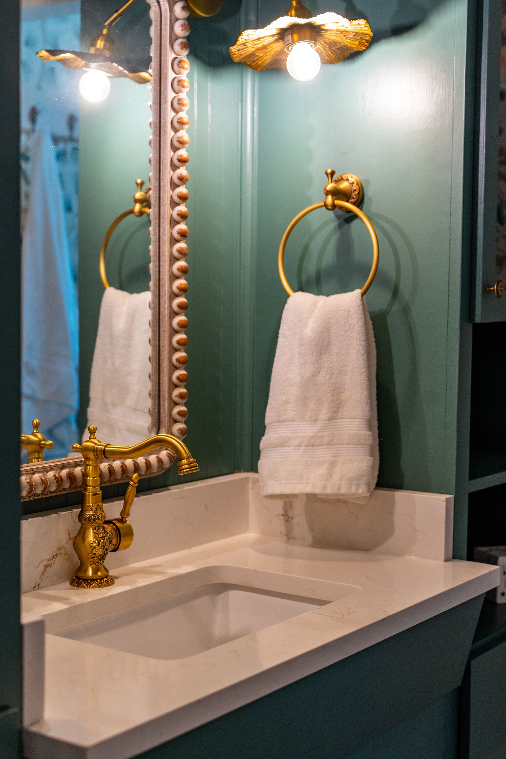 Een badkamer met een wit wastafelmeubel, gouden kraanwerk, een spiegel met decoratieve lijst en een handdoekhouder.