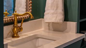 Een badkamer met een wit wastafelmeubel, gouden kraanwerk, een spiegel met decoratieve lijst en een handdoekhouder.