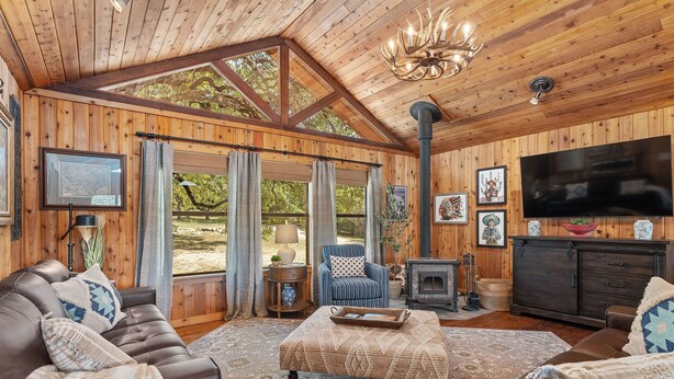 A cozy cabin interior with a wooden ceiling, a fireplace, a television, and a comfortable seating area.
