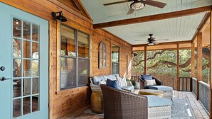 A covered porch with wicker furniture, a ceiling fan, and large windows.
