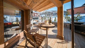 A wooden deck with a table and chairs, a stone wall, and a view of a snowy mountain town.