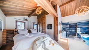 A modern bedroom with a large bed, wooden ceiling beams, and a bathroom with a blue marble wall.