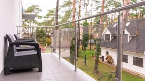 A balcony with a glass railing, a wicker chair, and a view of a residential area with trees and houses.