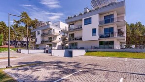 A multi-story residential building with balconies, a paved driveway, and a clear sky.