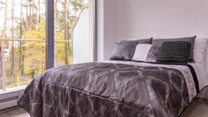 A bedroom with a large window, a bed with a patterned bedspread, and multiple pillows.