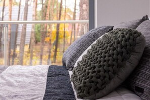 Una cama con muchas almohadas y vista a árboles a través de una ventana.