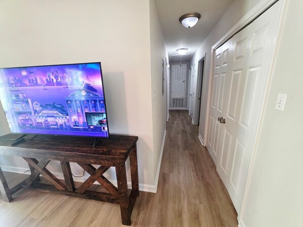 A hallway with a wooden table and a television displaying a cityscape.