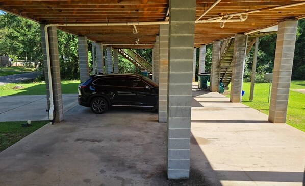A covered parking area with a car parked under a wooden roof structure.