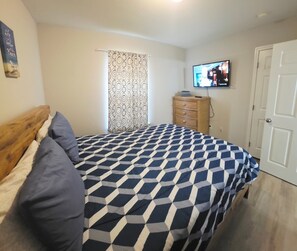 A bedroom with a bed, a dresser, a television, and a door.