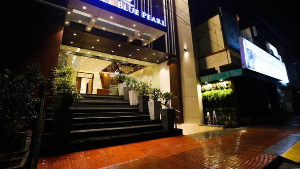 Exterior del Hotel Blue Pearl, con una entrada bien iluminada, una escalera que conduce al vestíbulo y un diseño arquitectónico moderno.