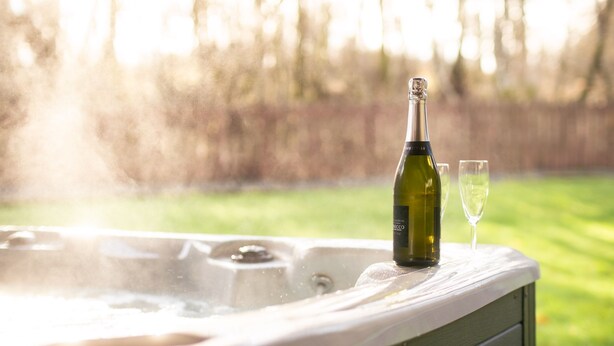 Un bain à remous avec une bouteille de vin et un verre posé sur le bord.