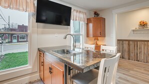 Een keuken met een groot raam, een flatscreen-tv, een spoelbak en een eethoek met stoelen.