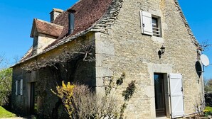 Una casa de piedra con techo inclinado, una chimenea y un ventanal con contraventanas.