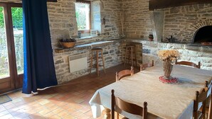 Cocina rústica de piedra con horno empotrado, taburetes de madera y una mesa de comedor para cuatro.