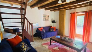 Un interior rústico con una escalera de madera, un sofá azul con cojines naranja, una mesa de centro de madera y una alfombra roja con estampado.