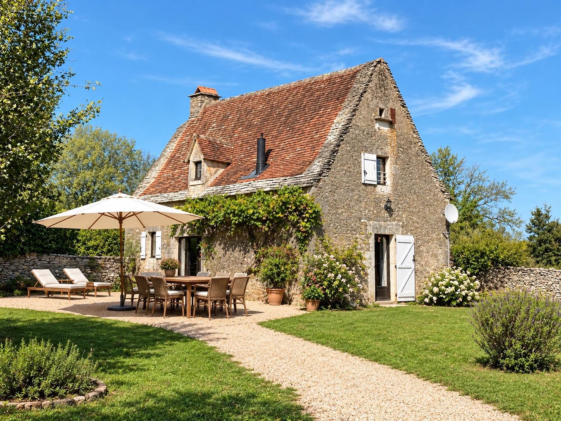 Une maison en pierre avec un toit en tuiles, une allée en gravier et une terrasse aménagée avec du mobilier d’extérieur.