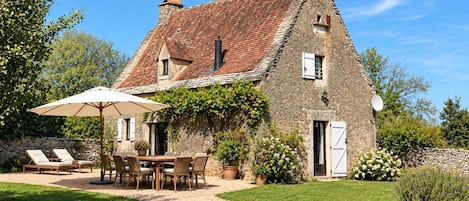 A stone house with a tiled roof, a gravel driveway, and a patio with outdoor furniture.