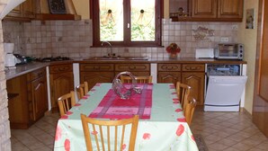 A kitchen with wooden cabinets, a tiled backsplash, a dining table with chairs, a coffee maker, a toaster, and a dishwasher. - Location Vacances des Quatre Vents (GIRMONT VAL D AJOL)