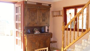 A dining area with a wooden cabinet, a table with a tablecloth, and a staircase. - Location Vacances des Quatre Vents (GIRMONT VAL D AJOL)