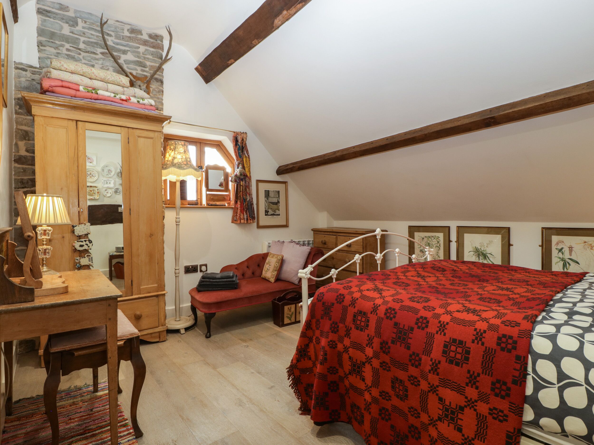 Un dormitorio acogedor con cama, un escritorio de madera, una silla, una lámpara y un aparador.