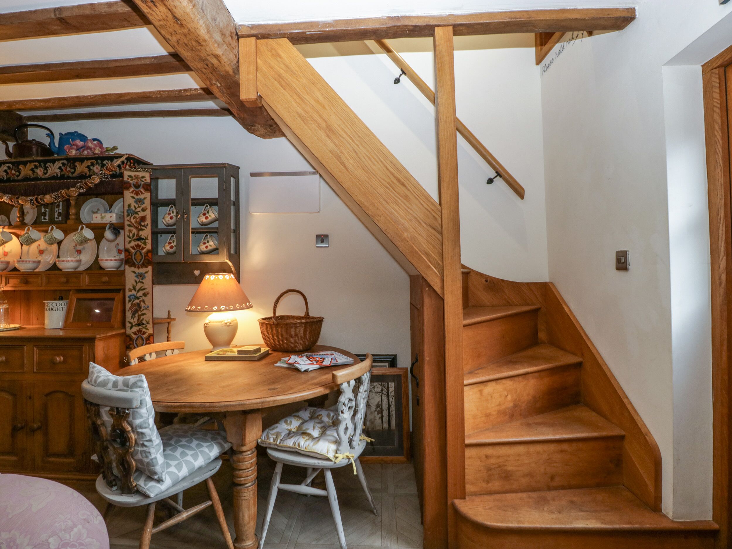 A wooden staircase leading to an upper floor, a dining area with a round table and chairs, and a kitchen area with cabinets and decorative items.