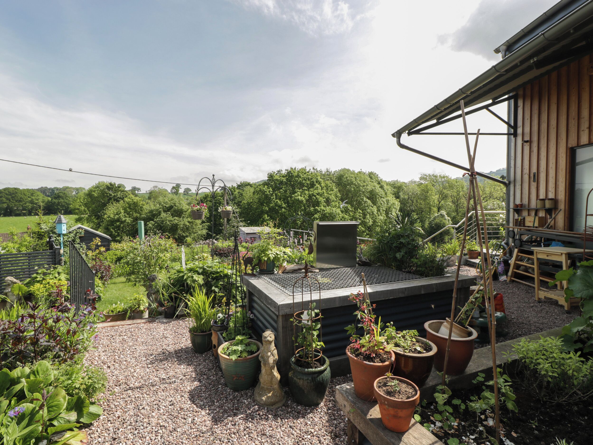 Un jardín en la azotea con plantas en macetas, un banco de madera y una estructura metálica.