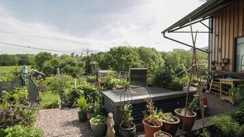 Un jardín en la azotea con plantas en macetas, un banco de madera y una estructura metálica.