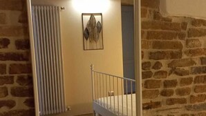 Ein Zimmer mit einem großen Spiegel, einem Bett, einem Heizkörper und einer Tür zu einem anderen Raum.