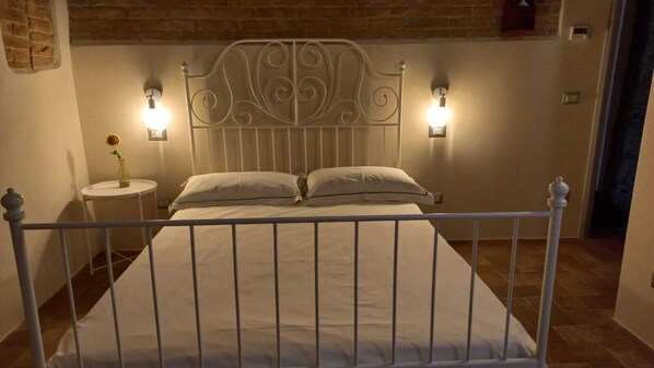 A bed with a metal headboard, two bedside lamps, and a small table with a vase of flowers. - Pagum Place (Torrita di Siena)