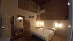 Ein Schlafzimmer mit Steinwand, einem Bett mit Metallkopfteil, einem Nachttisch mit Lampe und einem Spiegel.