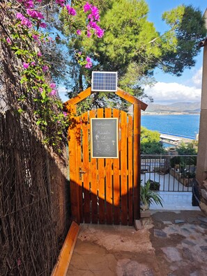 Ein hölzernes Tor mit einem Schild, das willkommen heißt, einer Solaranlage und Blick auf das Meer.
