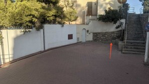 A paved courtyard with a white wall, a small door, and a staircase leading to a higher level.