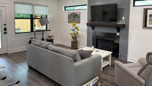 Ein modernes Wohnzimmer mit grauem Sofa, einem Couchtisch, einem Kamin und einem darüber montierten Fernseher.