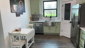 Eine kleine Küche mit Esstisch, weißen Stühlen, einer Edelstahl-Spüle und einem Kühlschrank.