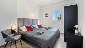 Une chambre moderne avec un grand lit, un fauteuil, une télévision et une fenêtre donnant sur un beau paysage.