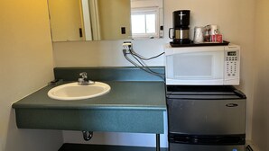 A bathroom with a sink, a mirror, a coffee maker, and a refrigerator.