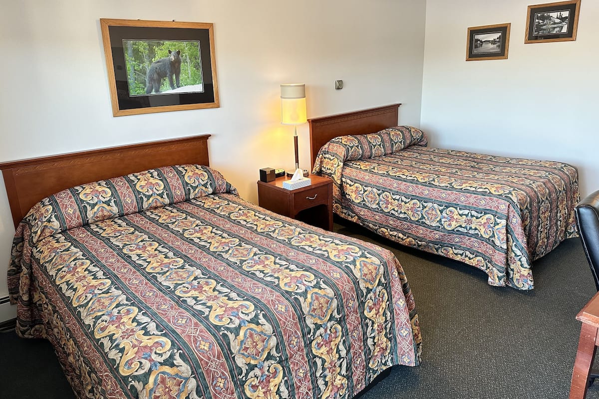 A hotel room with two beds, a nightstand with a lamp, and framed pictures on the wall.