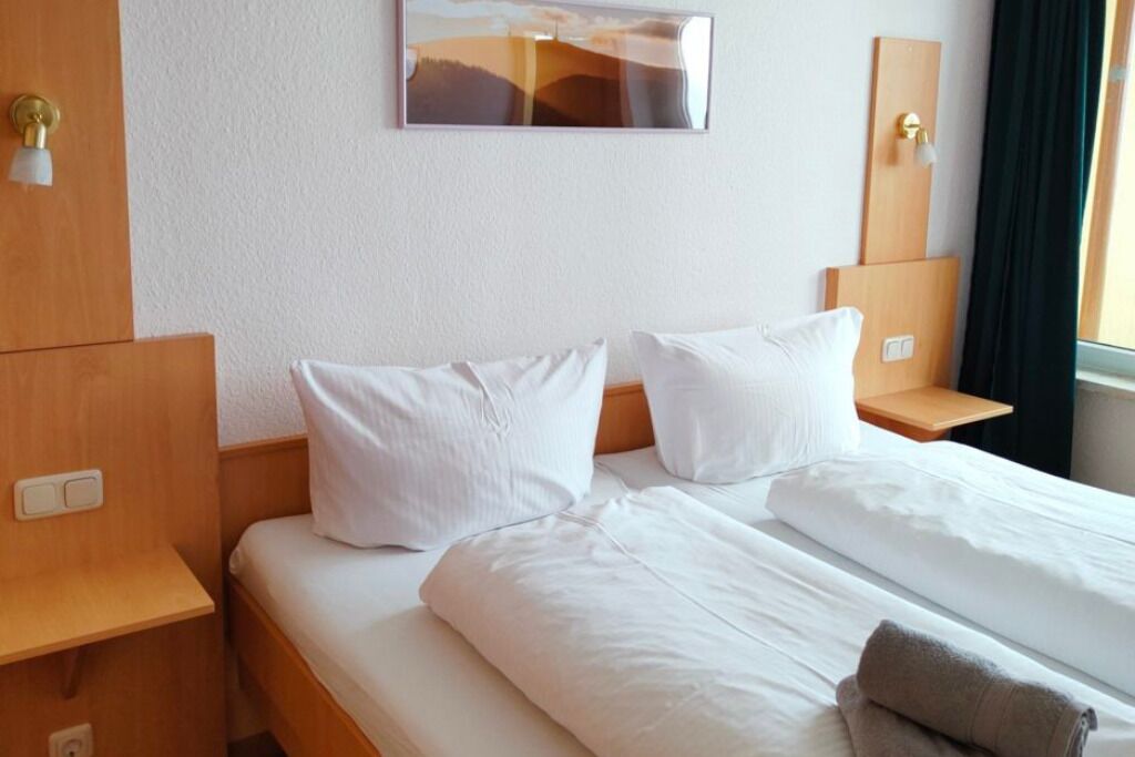 Ein Hotelzimmer mit einem Bett, zwei Nachttischen, einer Wandleuchte und einem mit Vorhängen versehenen Fenster.