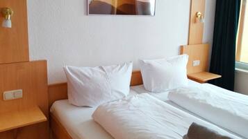 Ein Hotelzimmer mit einem Bett, zwei Nachttischen, einer Wandleuchte und einem mit Vorhängen versehenen Fenster.