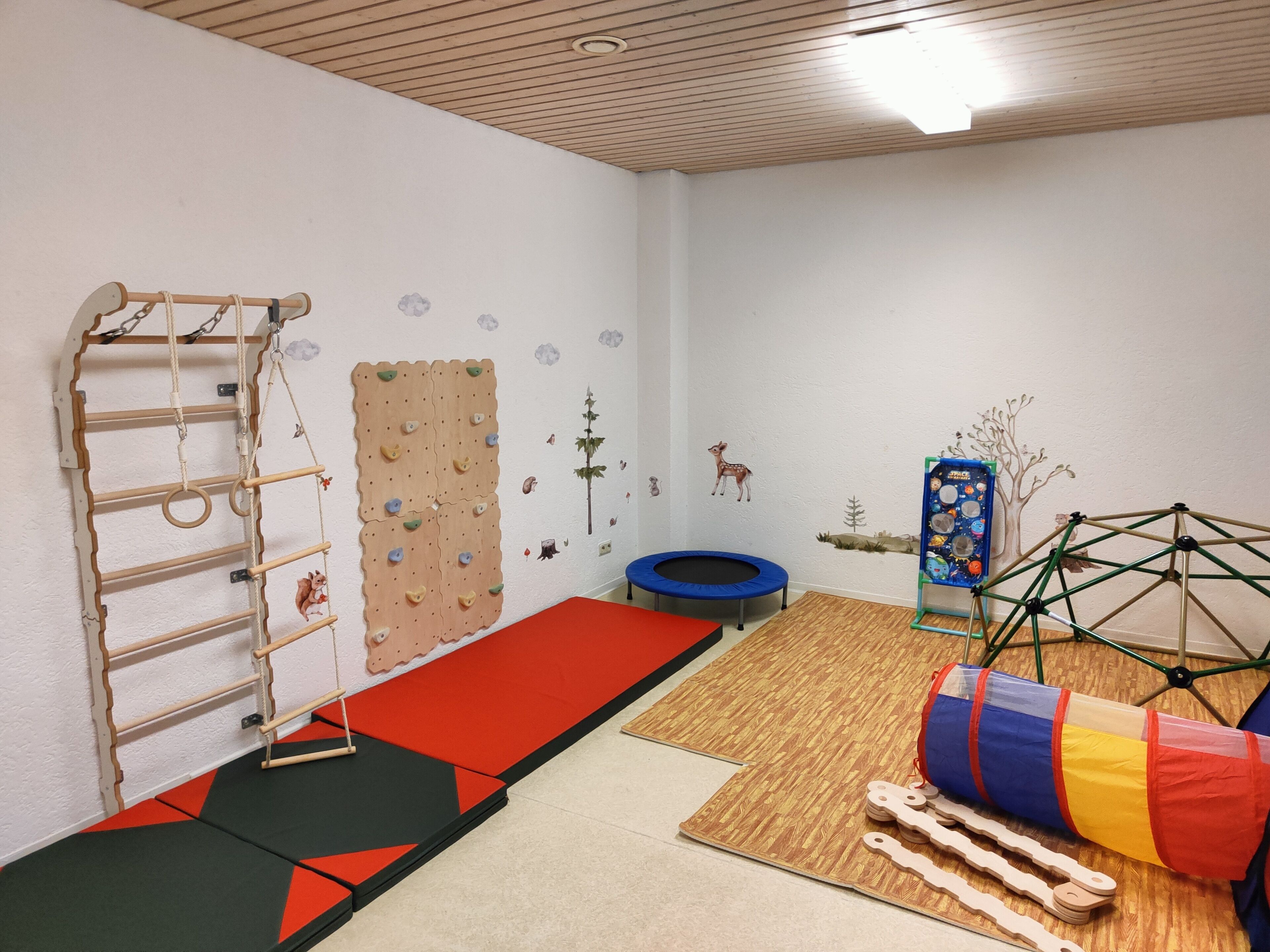 A room with a climbing wall, a trampoline, and a play area with a ball pit and wooden structures.