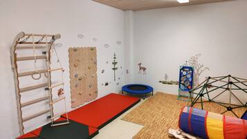 A room with a climbing wall, a trampoline, and a play area with a ball pit and wooden structures.