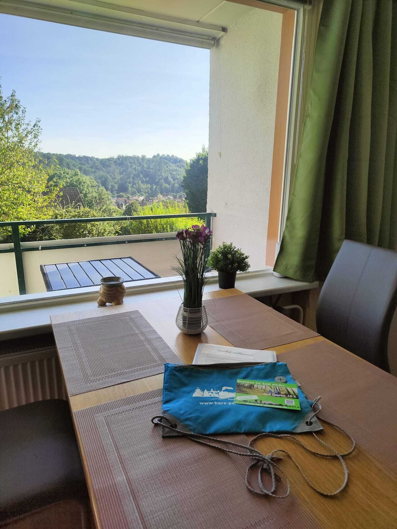 A balcony with a view of a green landscape, a table with a mat, a plant, and a bag.