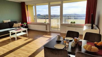 A modern living room with a dining area, large windows with a view of a distant landscape, a sofa, a coffee table, and a dining table set for a meal.