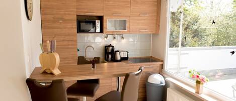 A modern kitchen with wooden cabinets, a microwave, a coffee maker, and a window with a view of trees.