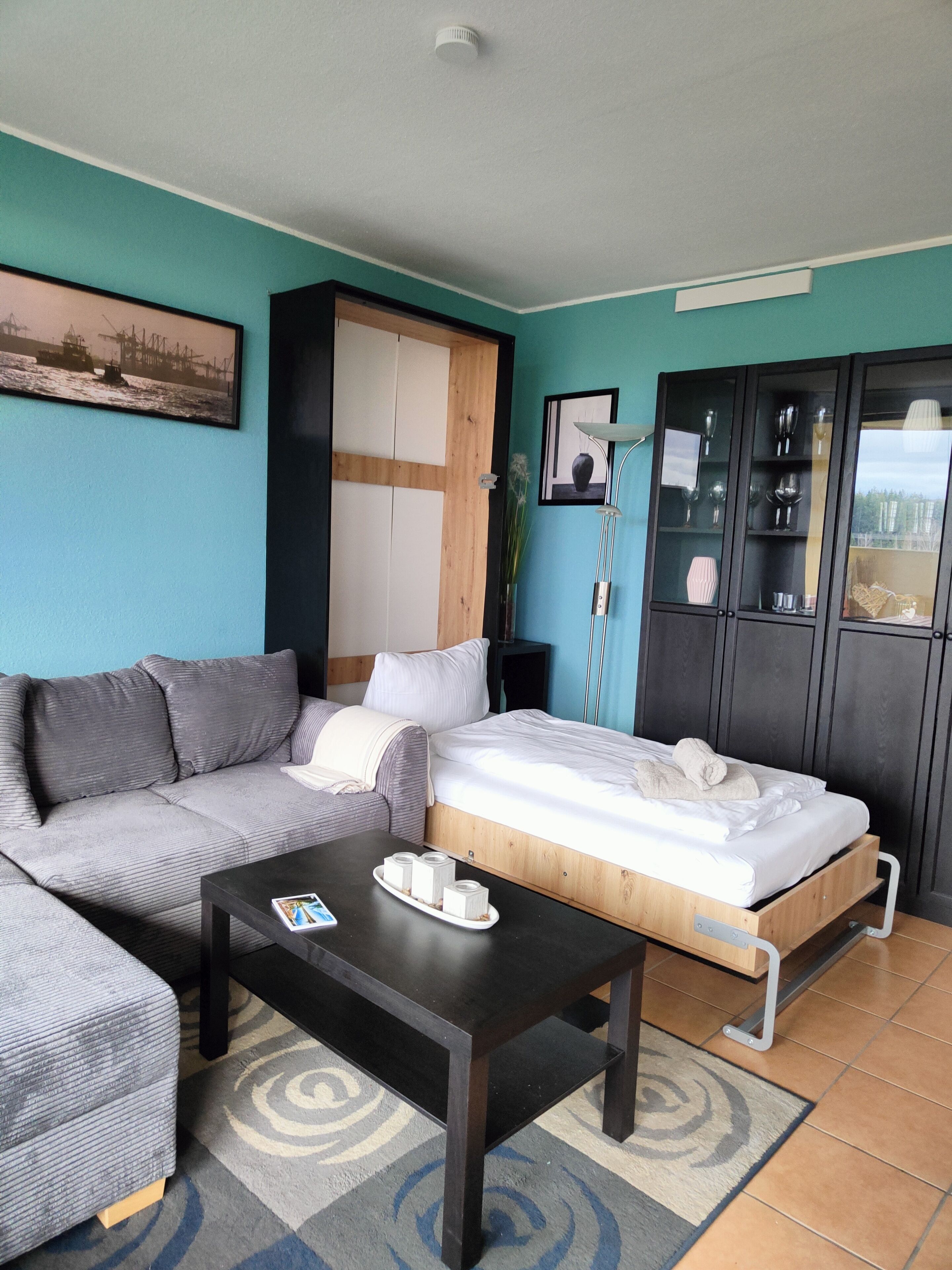 Una sala moderna con sofá, cama, mesa de centro y un aparador con puertas de vidrio.