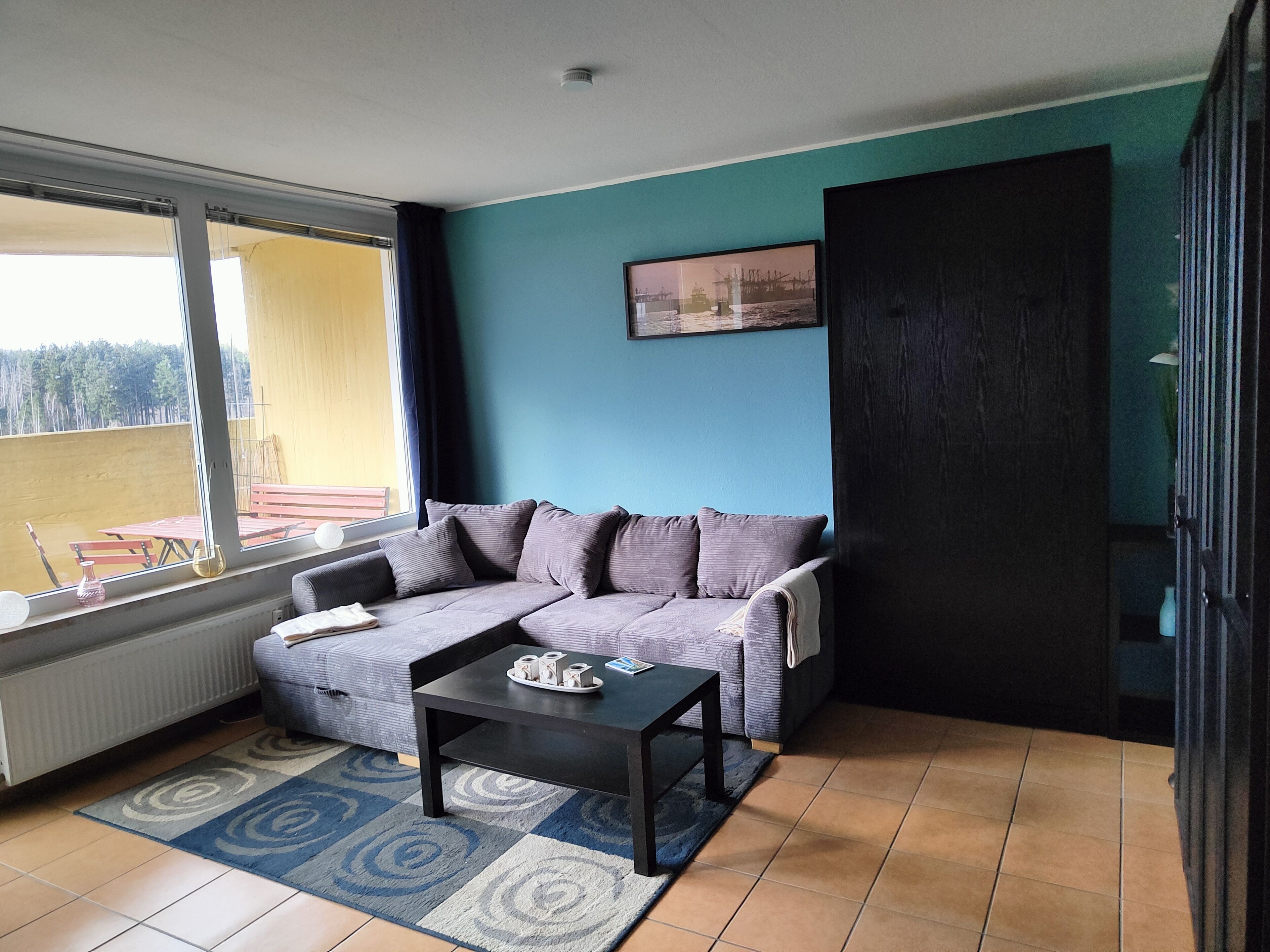 Una sala moderna con un sofá gris, una mesa de centro negra y una alfombra azul y gris con estampado.
